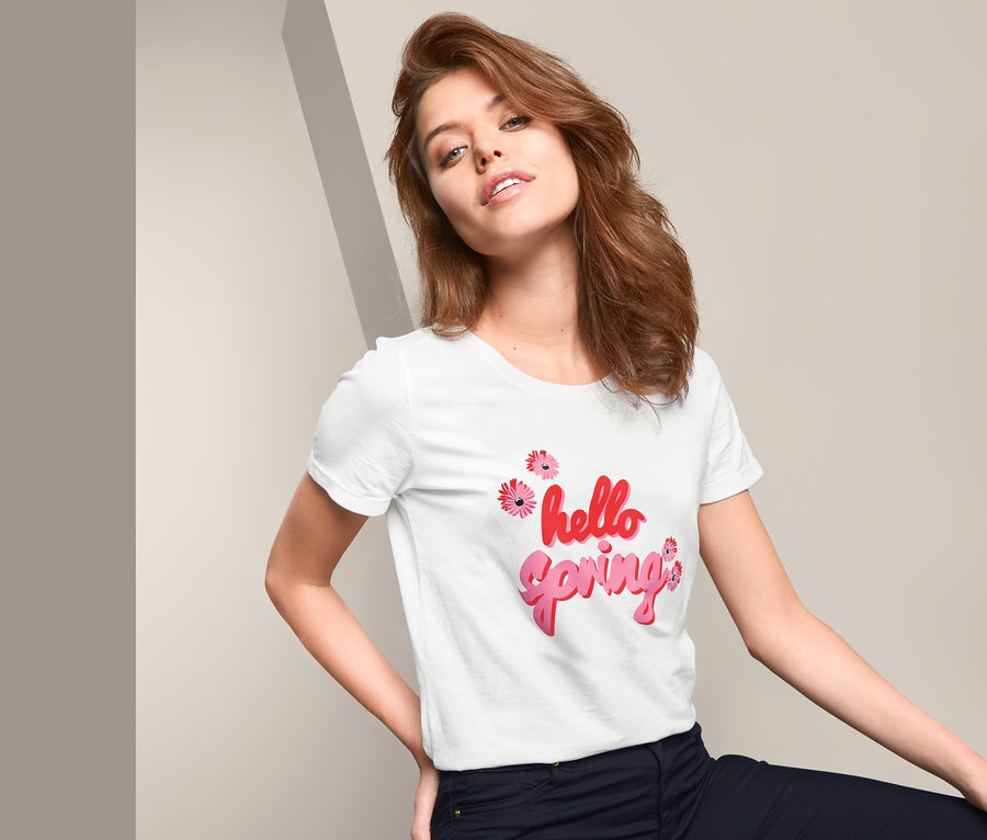 Frau sitzt und trägt ein weißes Kurzarmshirt mit Wording-Print "hello spring".