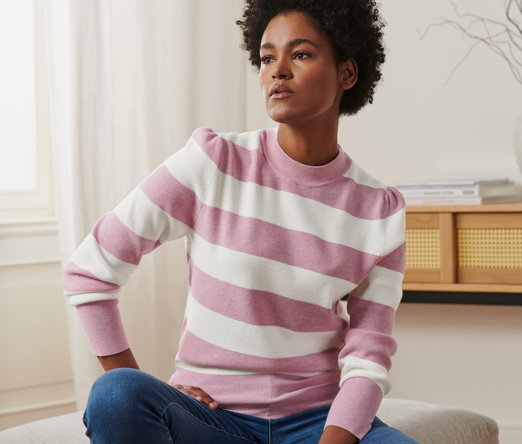 Frau sitzt und trägt einen Pullover mit Puffärmeln und Jeans.