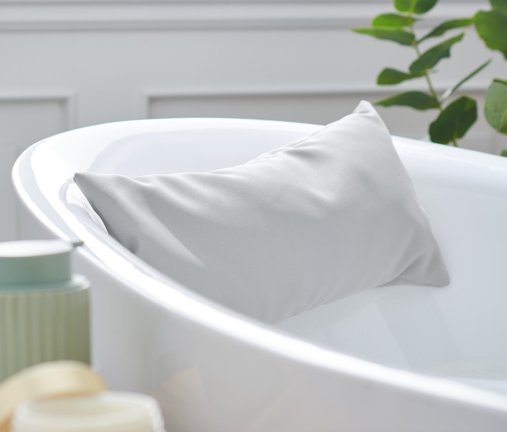 Ein graues Badewannenkissen lehnt an einem weißen Badewannenrand.