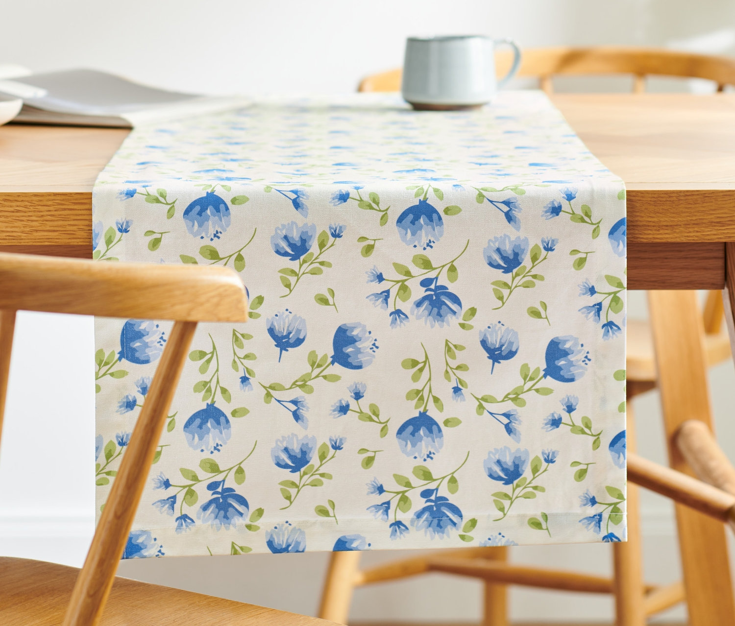 Ein Baumwoll-Tischläufer mit Blütenmuster liegt auf einem Holztisch.