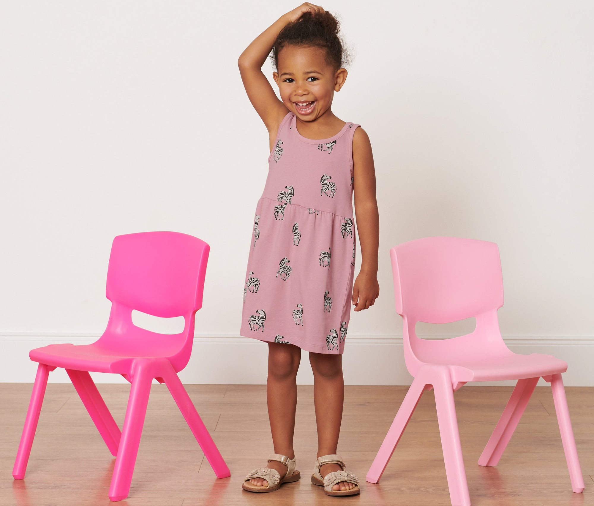 Ein lächelndes Mädchen steht zwischen zwei rosa Stühlen und trägt ein Kinder-Jerseykleid mit Zebra.