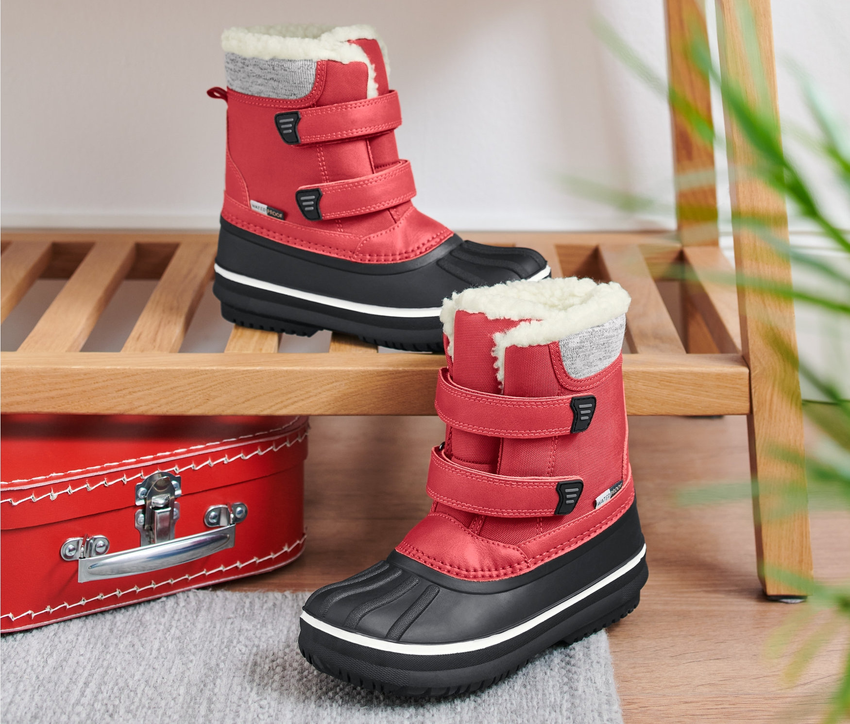 Zwei rote Kinder-Allwetterstiefel stehen auf einem Holzregal.