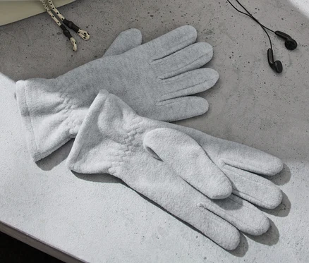 Zwei graue Fleece-Handschuhe liegen auf einer grauen Oberfläche neben Kopfhörern und einer Tasche.