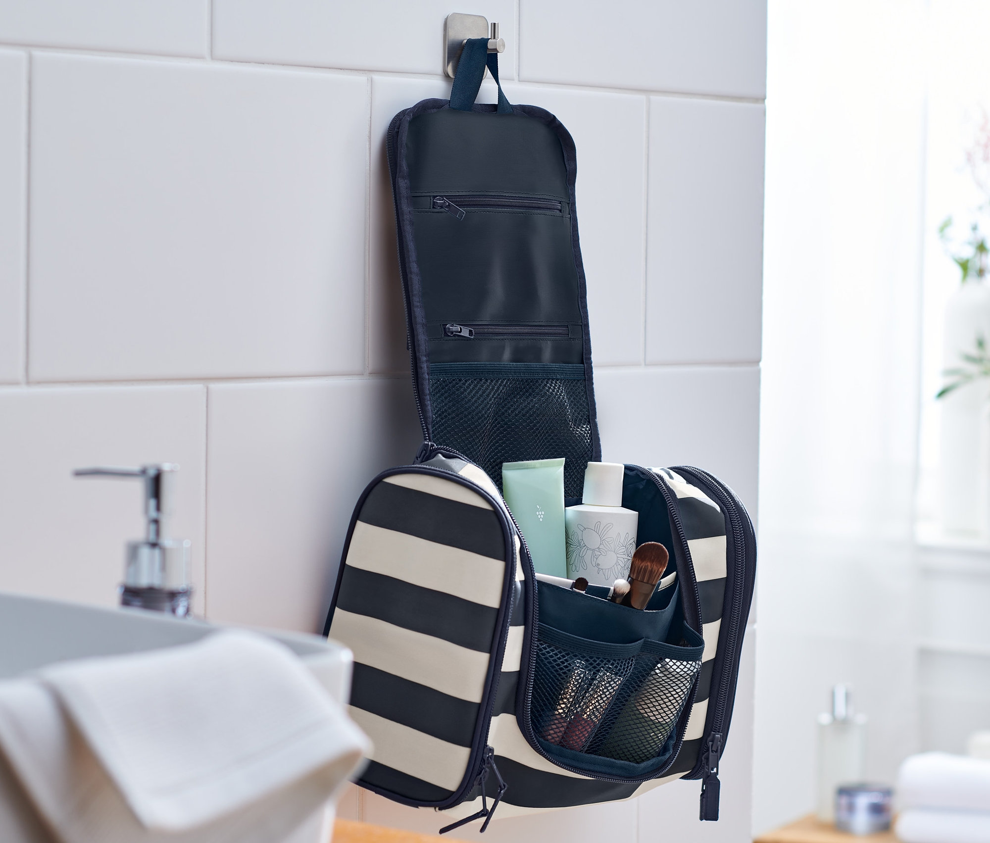 Eine gestreifte Kulturtasche hängt offen an einer Badezimmerwand.