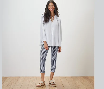 Frau steht und trägt eine weiße Bluse und bedruckte 3/4-Leggings.