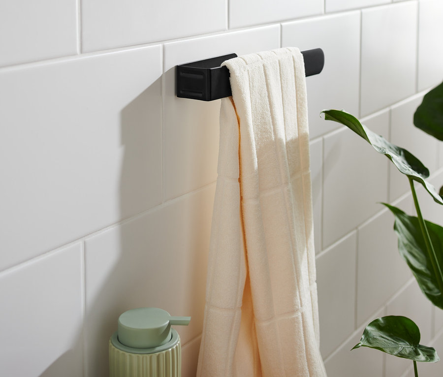 An weißen Fliesen hängt ein schwarzer Handtuchhalter mit einem cremefarbenen Handtuch.