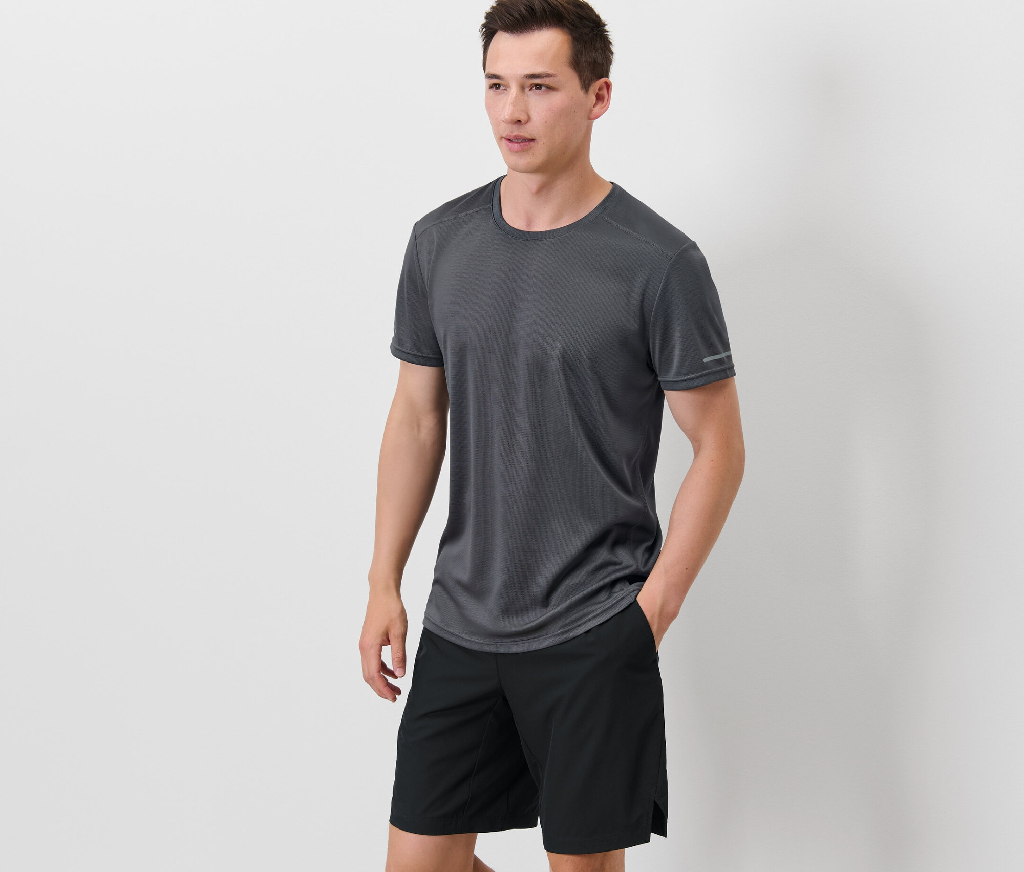 Mann steht mit Händen in den Taschen seiner schwarzen Shorts, er trägt ein graues Funktionsshirt.