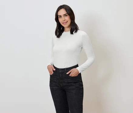 Frau mit Händen in den Taschen dunkler Jeans und weißem Langarmshirt.