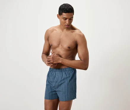 Mann mit freiem Oberkörper reibt seine Hände; er trägt blau gestreifte Boxershorts.