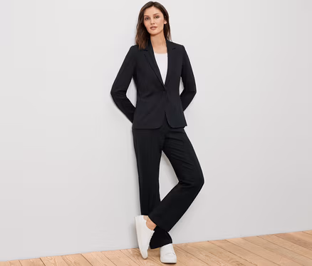 Frau posiert in schwarzem Jerseyblazer, schwarzer Hose und weißen Turnschuhen.