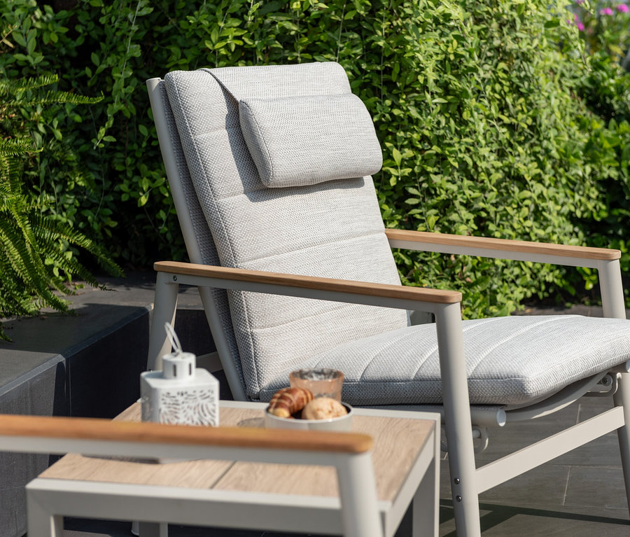 Detailaufnahme eines hellgrauen ScanCom Outdoor-Loungesessels mit verstellbarer Rückenlehne und Tisch mit Speisen.