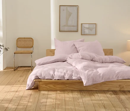 Rosafarbene Leinen-Bettwäsche in Übergröße liegt auf einem Holzbett.