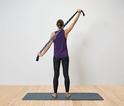 Frau dehnt den Oberkörper mit einem Yogagurt.