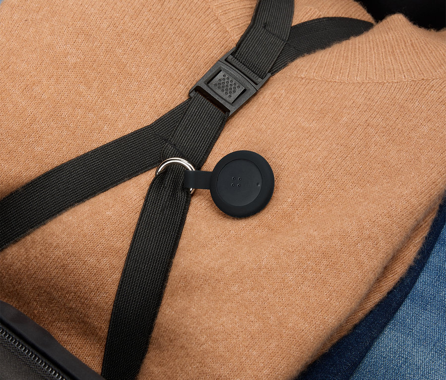 Ein brauner Pullover und blaue Jeans liegen in einem Koffer, darüber ein schwarzer Gurt mit einem runden, schwarzen Anhänger.