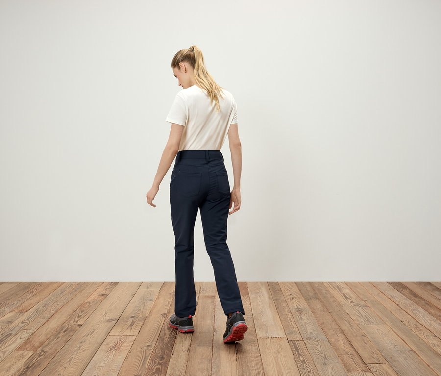 Von hinten ist eine Frau mit blonden Haaren im Pferdeschwanz, einem weißen T-Shirt, dunkelblauen Hosen und Turnschuhen zu sehen.