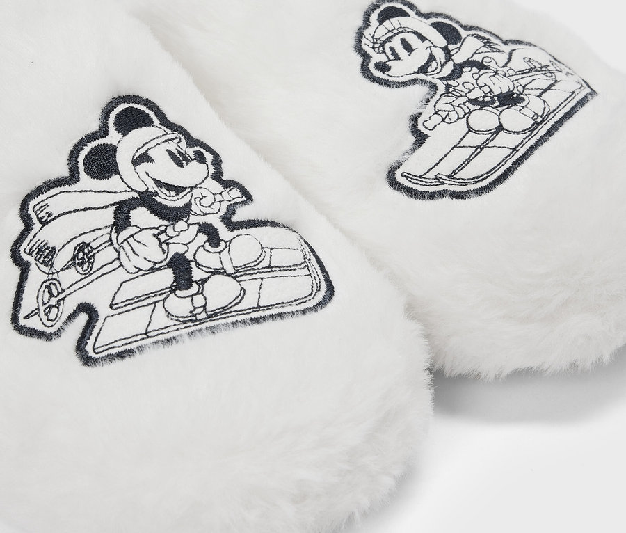 Detail von weißen, flauschigen Hausschuhen mit gezeichneten Bildern von Mickey Mouse auf einem Schlitten.