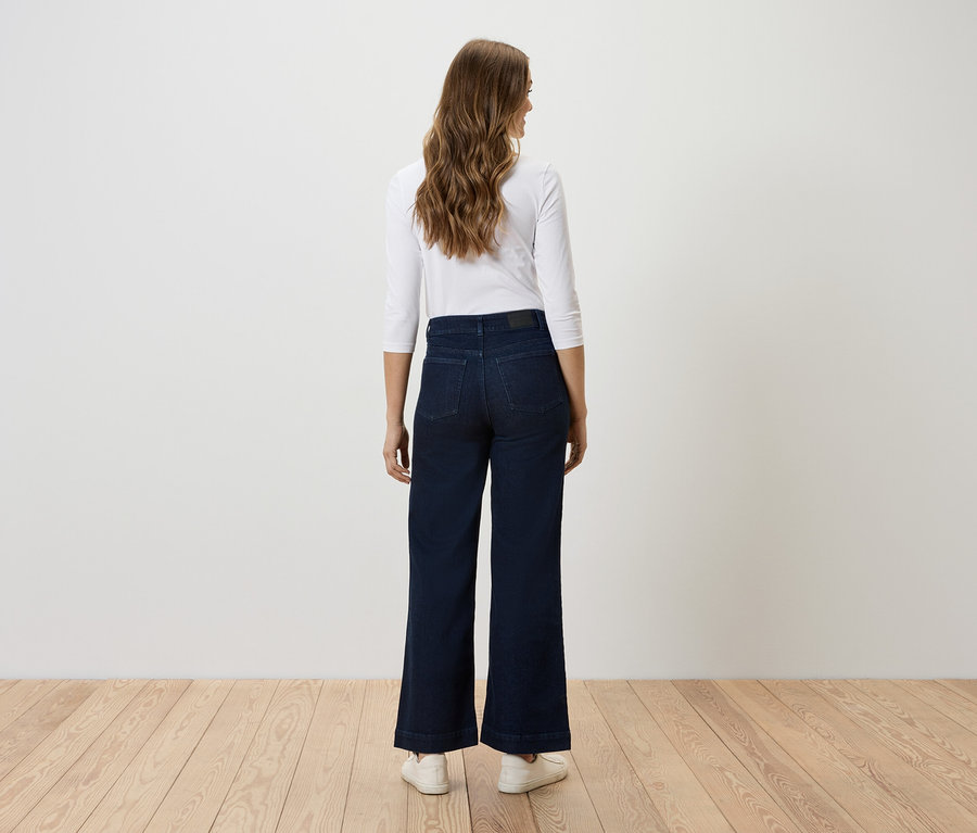 Frau steht mit dem Rücken zur Kamera und trägt dunkelblaue, weite Jeans und ein weißes Oberteil.