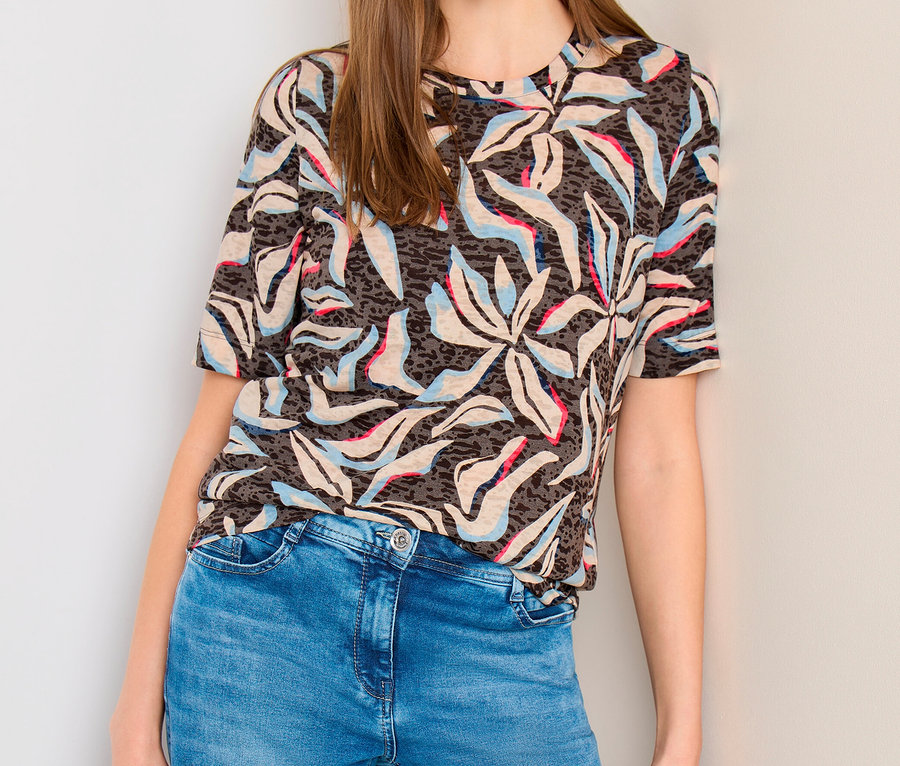 Frau trägt CECIL Kurzarmshirt mit blau-rosa-beigem Muster, blaue Jeans, hält schwarze Tasche.
