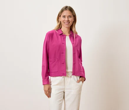 Frau trägt eine pinke Jacke über einem weißen Oberteil und cremefarbene Hosen.
