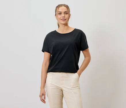 Frau mit schwarzem T-Shirt und beigen Hosen, die in die Kamera lächelt.