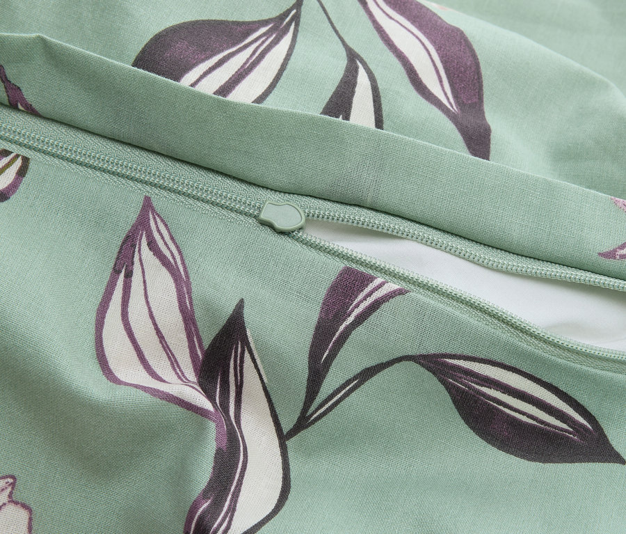 Nahaufnahme eines mintgrünen Kissenbezugs mit Reißverschluss und lila Blättermuster.