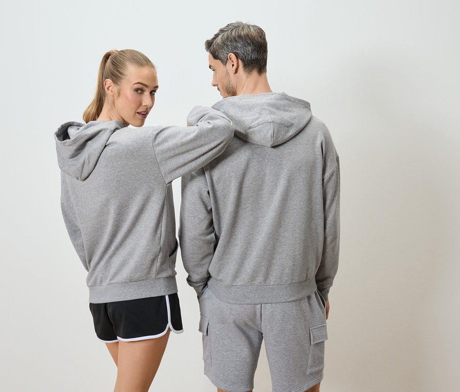 Frau mit blonden Haaren und Mann mit grauen Haaren tragen graue Kapuzenpullover und Shorts.