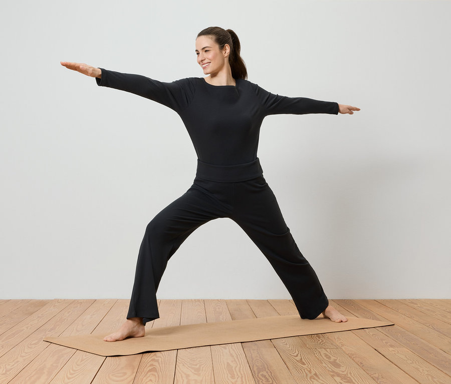 Eine Frau in schwarzer Sportbekleidung macht Yoga auf einer Yogamatte.