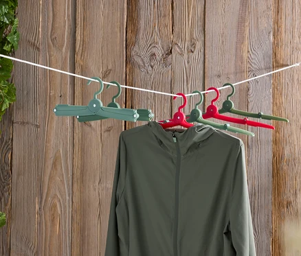 Eine grüne Jacke hängt an farbigen Kleiderbügeln an einer Wäscheleine vor einer Holzwand.