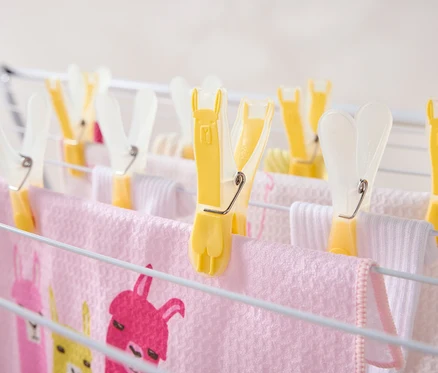 Mehrere gelbe Wäscheklammern halten rosa und weiße Handtücher auf einem Wäscheständer.