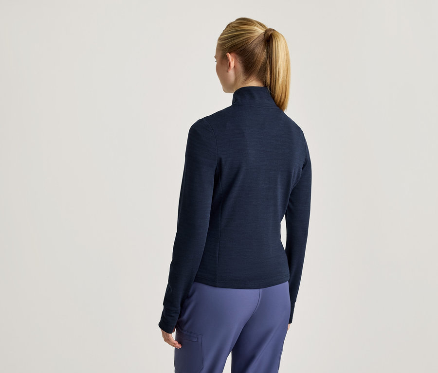 Von hinten ist eine Frau mit blondem Pferdeschwanz in einer marineblauen Jacke mit Reißverschluss und blauen Hosen zu sehen.