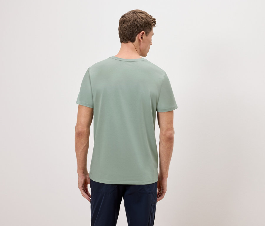 Ein Mann steht mit dem Rücken zur Kamera und trägt ein grünes T-Shirt und eine blaue Hose.