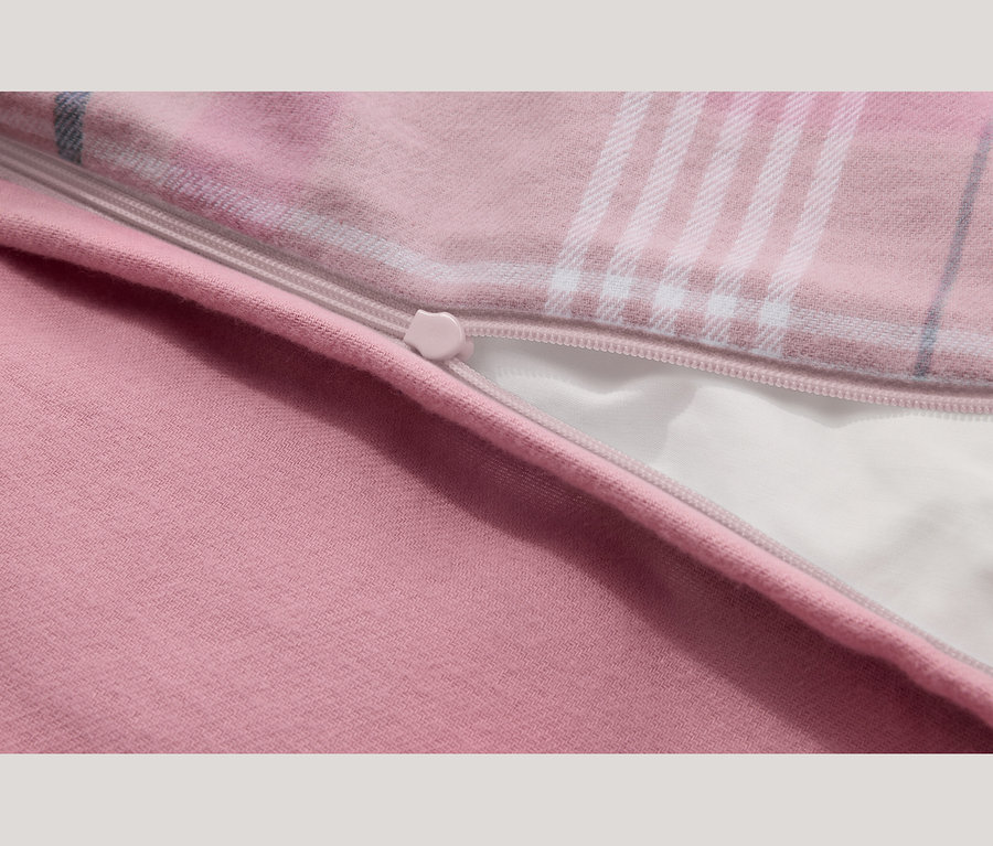 Nahaufnahme eines rosa Stoffes mit teilweise geöffnetem Reißverschluss. Der Stoff zeigt einen einfarbigen rosa Bereich und ein rosa Karomuster mit weißen und blauen Linien, das ein weißes Futter unter dem Reißverschluss enthüllt.