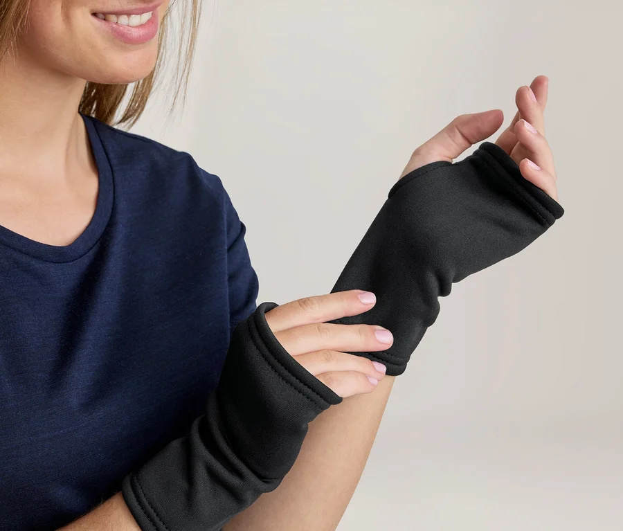 Lächelnde Frau in marineblauem Oberteil, die schwarze fingerlose Handschuhe trägt und einen davon anpasst.