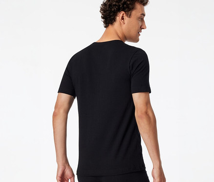 Mann von hinten, leicht zur Seite gedreht, trägt ein schwarzes SCHIESSER T-Shirt und schwarze Unterwäsche.