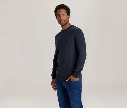 Mann in dunkelblauem Pullover und Jeans, eine Hand in der Hosentasche.