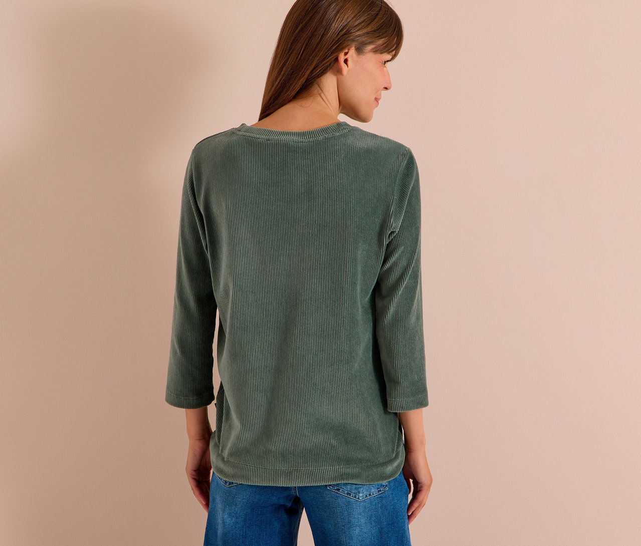 Frau von hinten, leicht zur Seite gedreht, trägt ein grünes CECIL 3/4-Cordshirt und blaue Jeans.