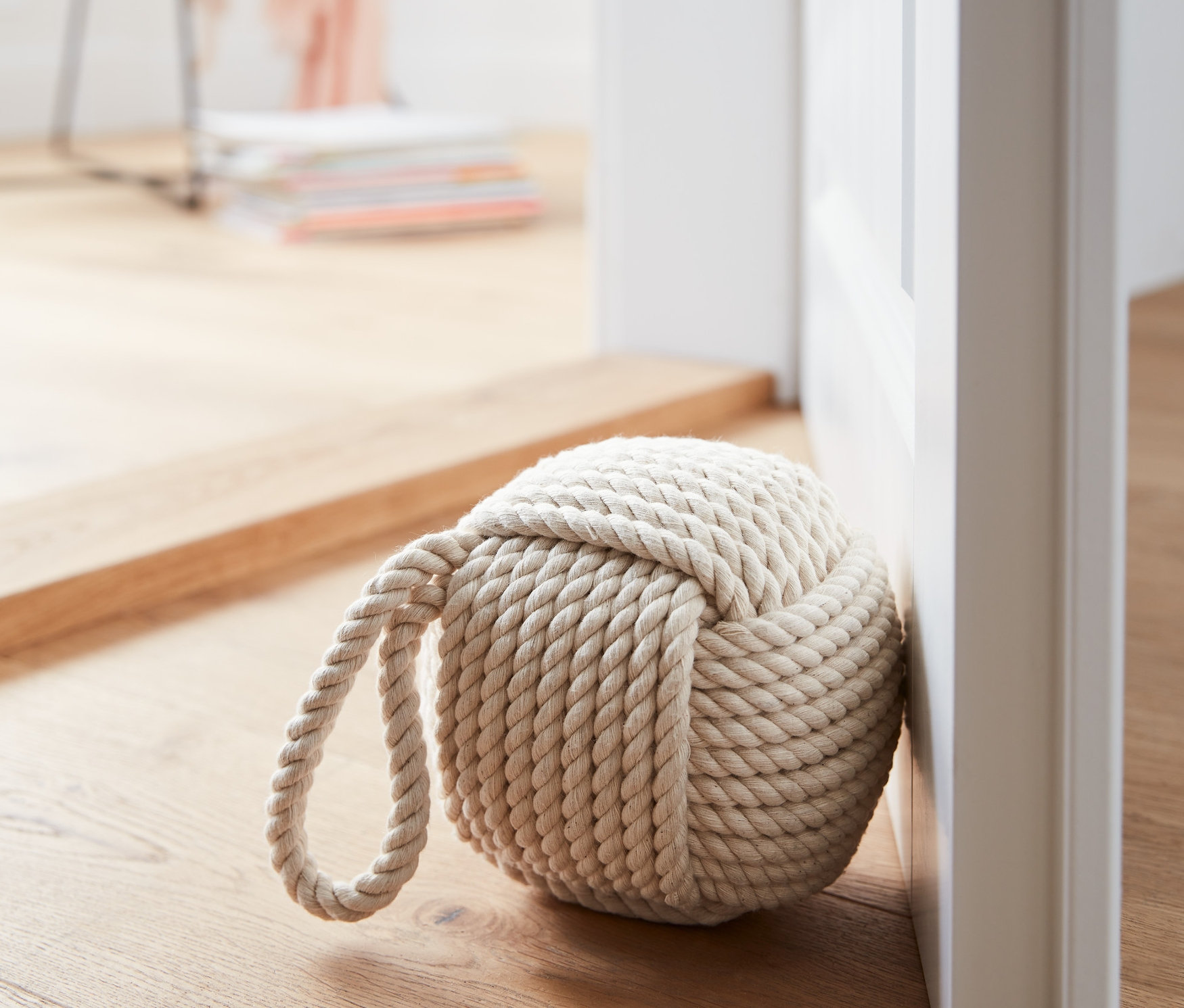Ein Türstopper aus Seil liegt an einer weißen Tür auf einem Holzboden.