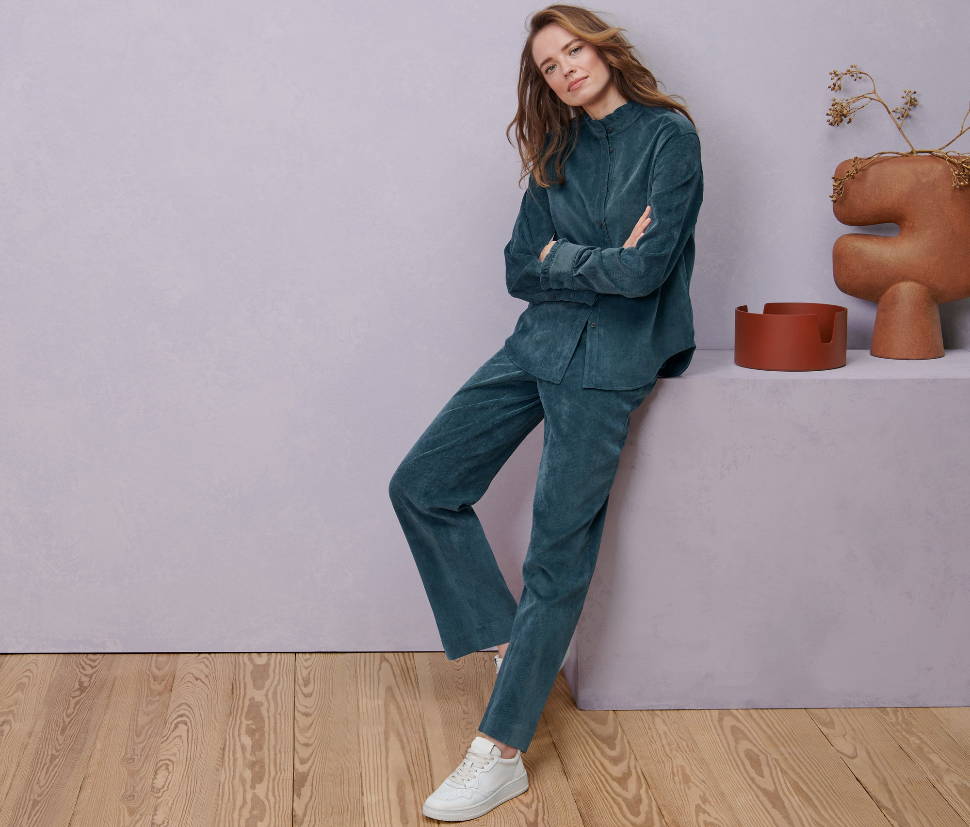 Frau posiert in Cordbluse mit Rüschendetail und rauchblauer Cordhose.
