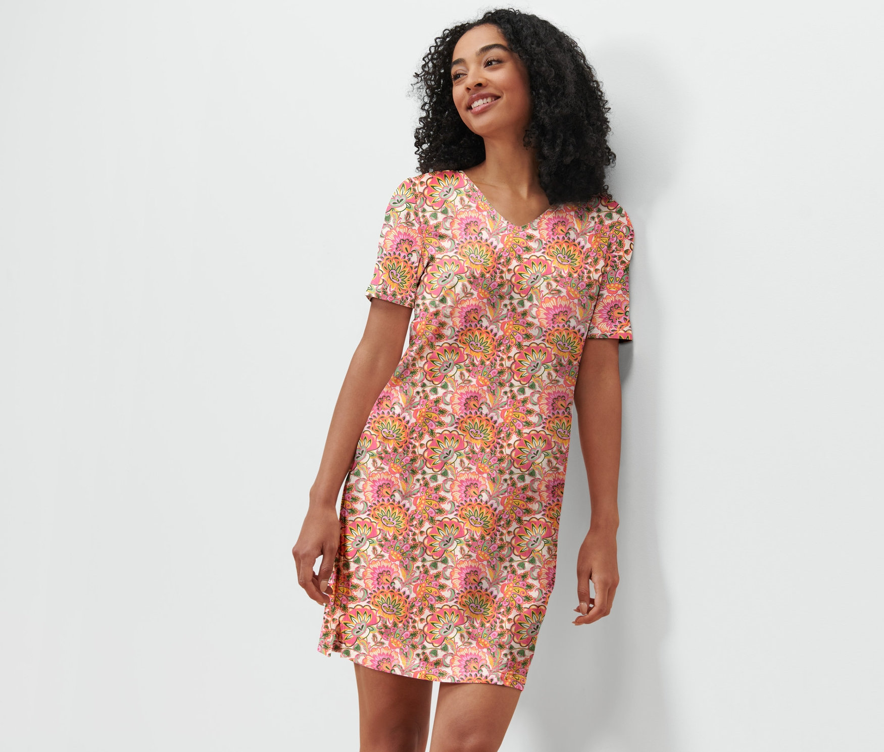 Frau lehnt an einer weißen Wand und trägt ein Nachthemd mit Blumenmuster.