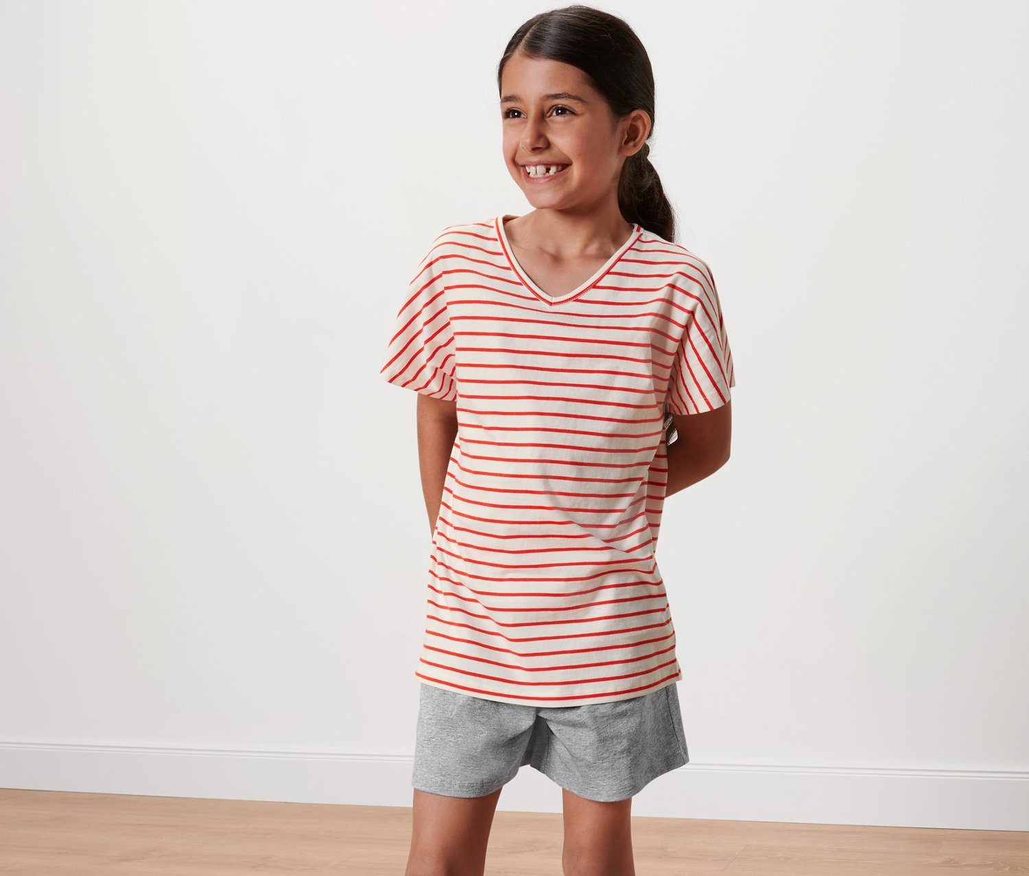 Lächelndes Mädchen im kurzen Kinder-Pyjama mit roten Streifen.