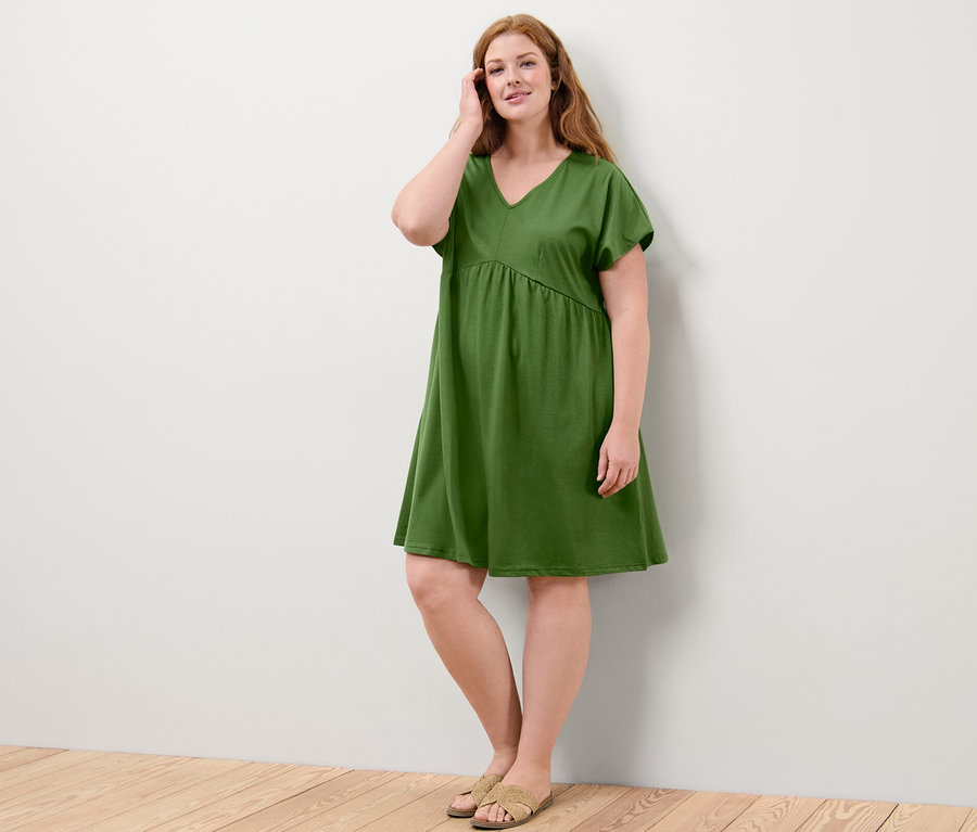 Eine Frau steht an einer Wand und trägt ein grünes Jerseykleid.