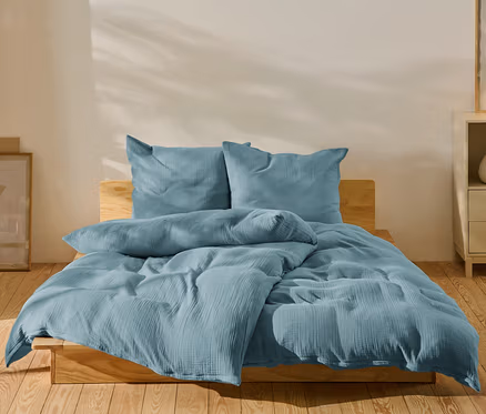 Blaue Musselin-Bettwäsche in Normalgröße und Übergröße auf einem Bett.