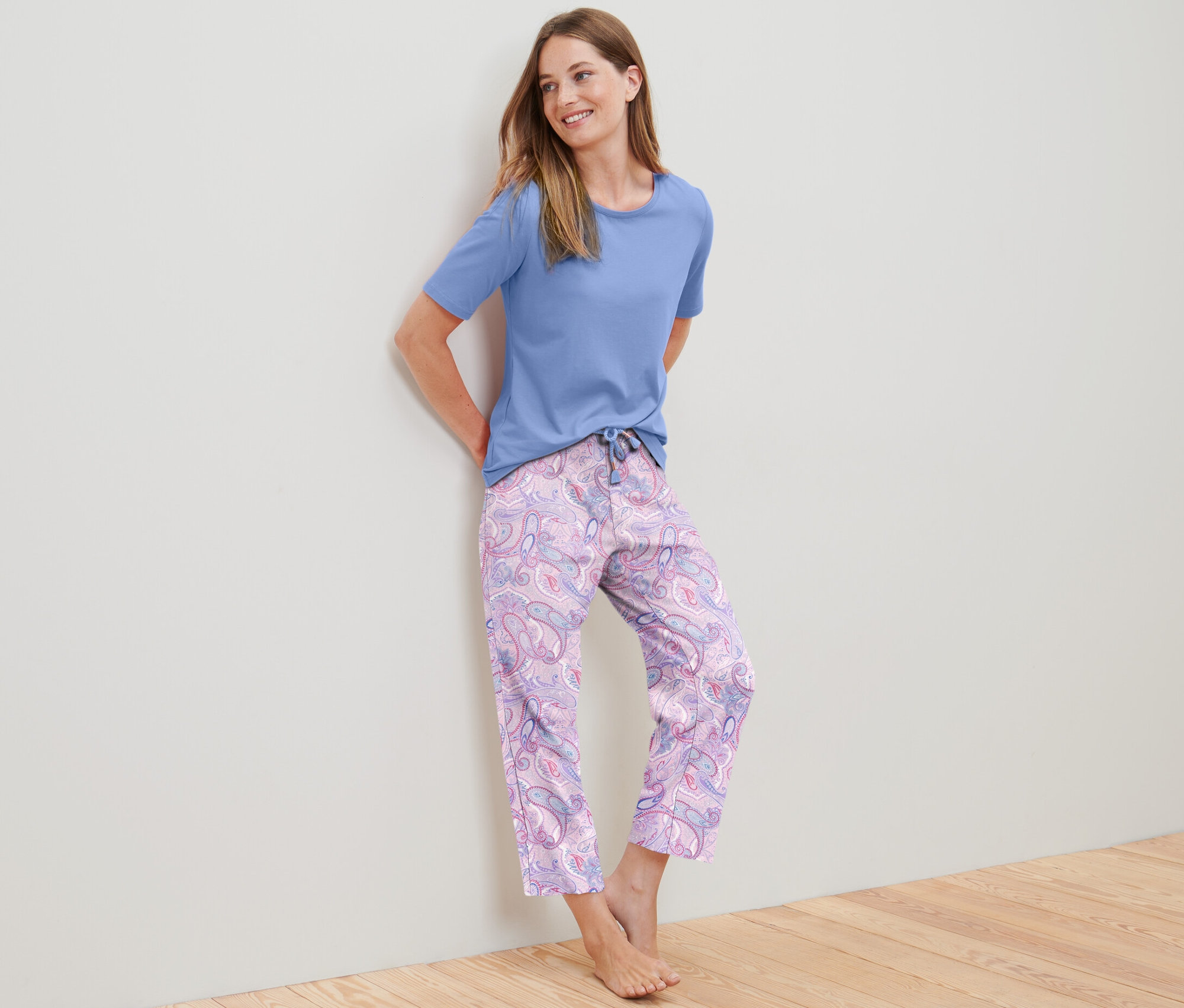 Eine Frau, die sich an eine Wand lehnt, trägt ein 7/8-Pyjama-Set.