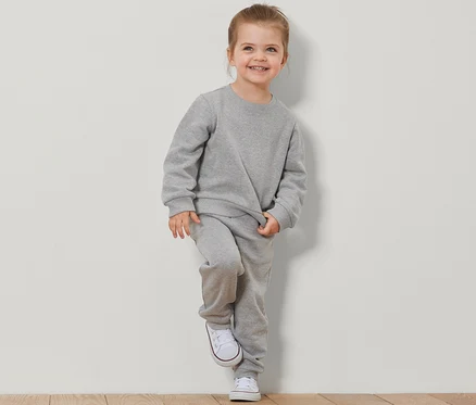 Lächelndes Mädchen lehnt an einer Wand in einem grauen 2 Kinder-Sweatshirts mit angerauter Innenseite Set.