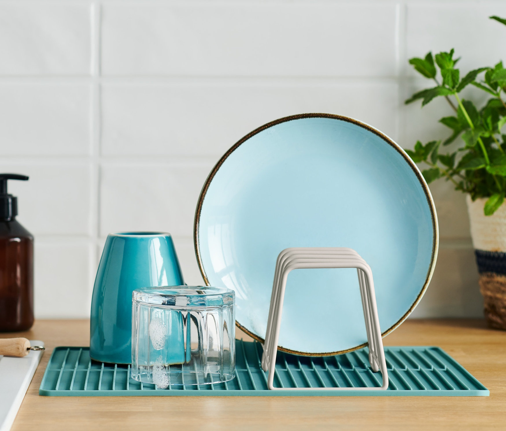 Blauer Teller, Glas und Abtropfgestell mit Silikonmatte auf einer Küchentheke.