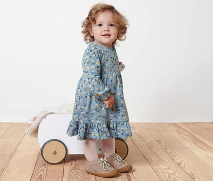 Mädchen steht neben einem weißen Wagen und trägt ein Baby-Jerseykleid.