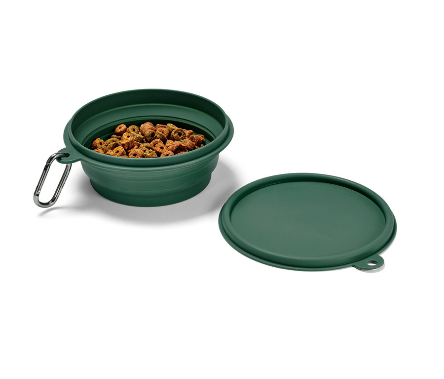 Ein grüner, faltbarer Fressnapf, gefüllt mit Trockenfutter, mit Karabinerhaken und einem Deckel daneben.