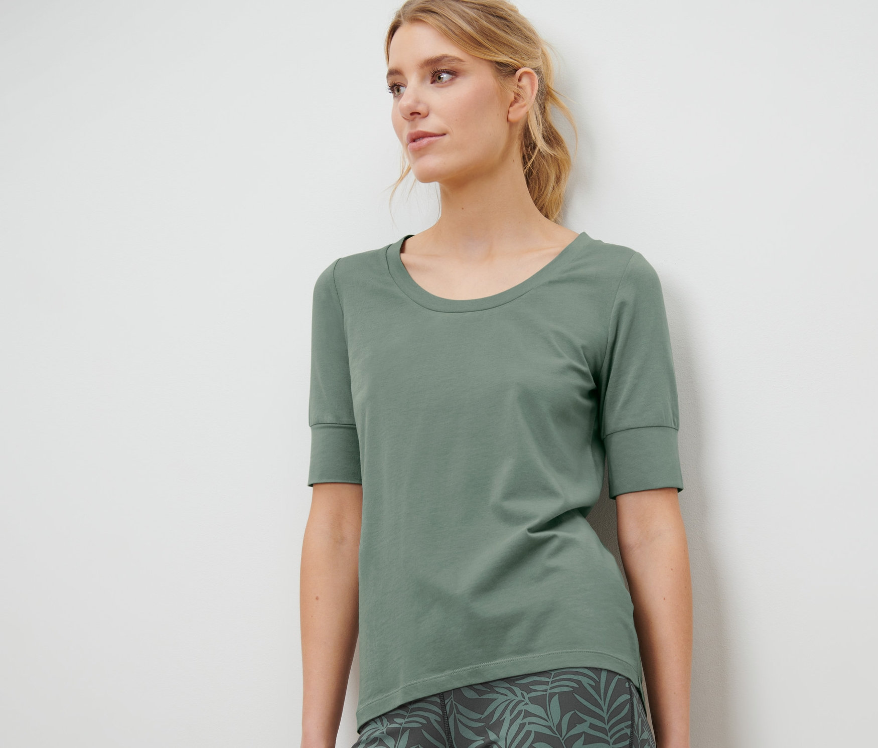 Eine Frau trägt ein grünes Funktionsshirt, halbarm, und Leggings mit Blätterdruck.