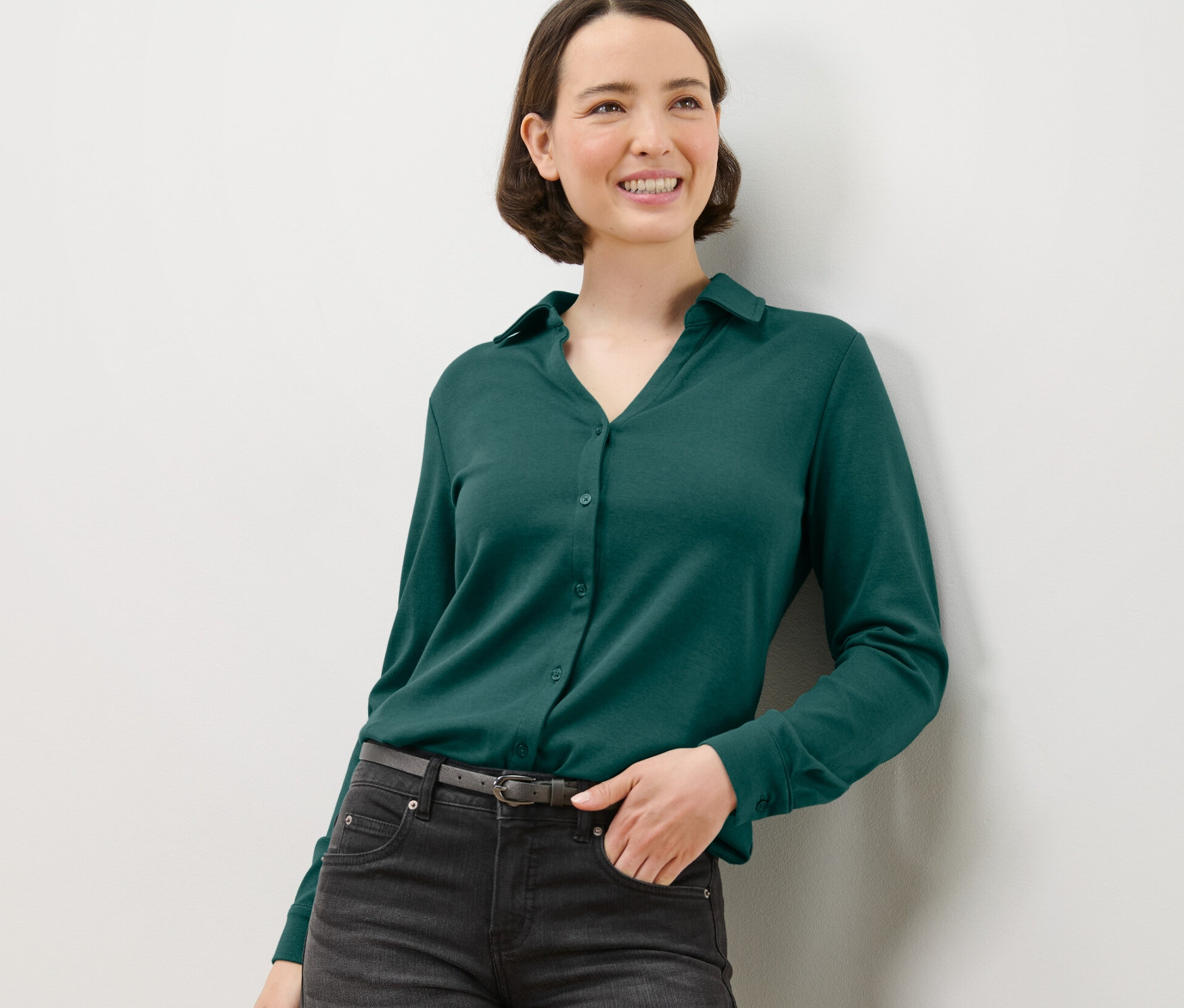 Frau posiert in grünem Blusenshirt mit Knopfleiste.