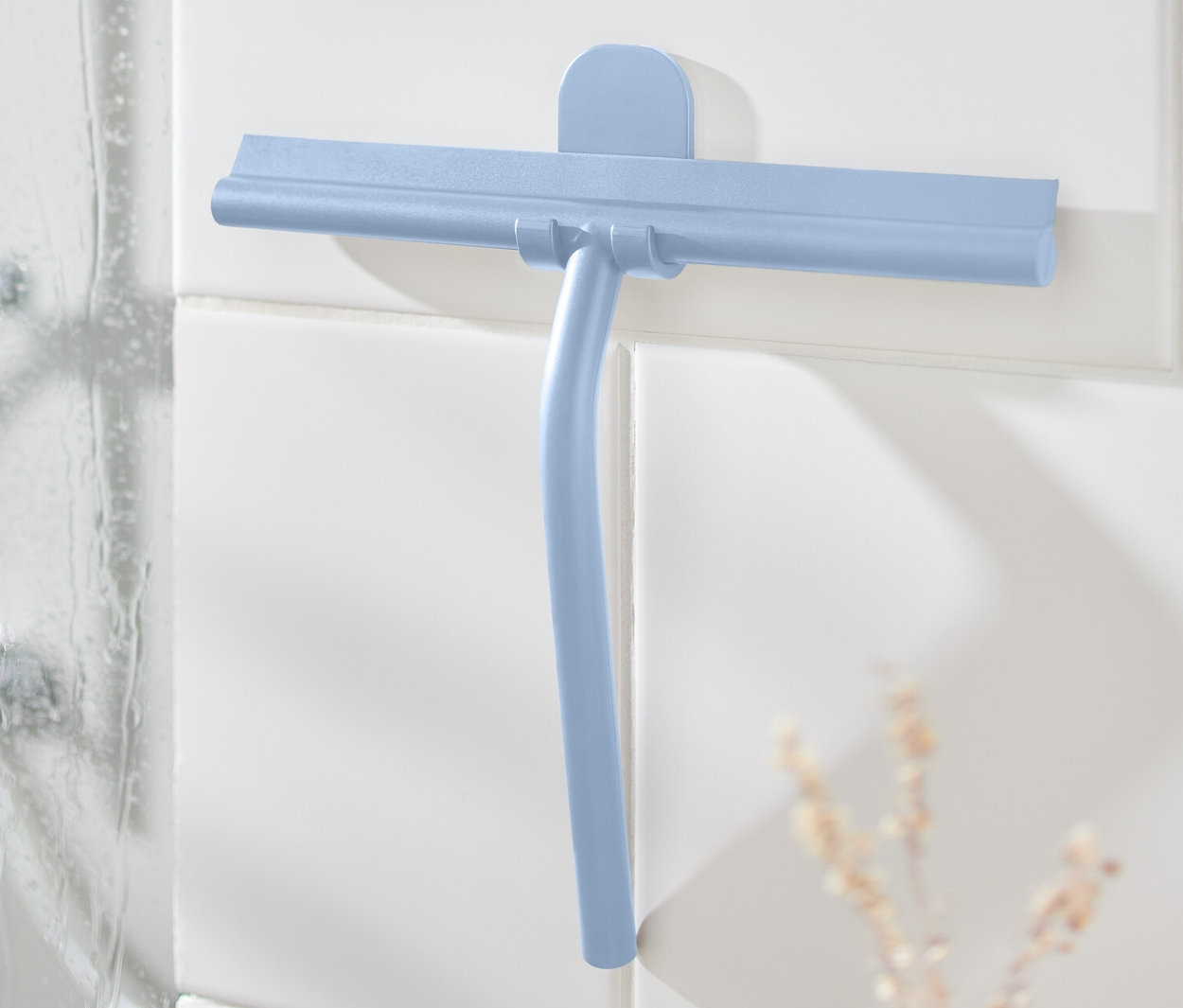 Blauer Badwischer mit Wandhalterung an weißen Fliesen neben der Dusche.